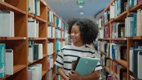 American student holding a book, walking between the shelves and selecting books for research in the library. Education, Knowledge, Learning concept