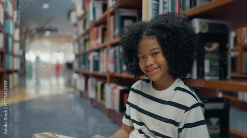American elementary student sitting on the floor in the library while studying and reading a book. Education, Learning and knowledge concept