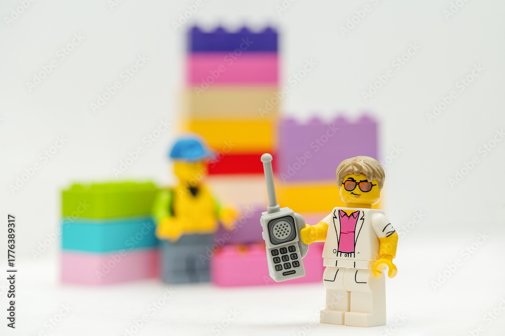 Naklejka premium Lego minifigure businessman with mobile phone standing next to multi-colored bricks. Studio shot.