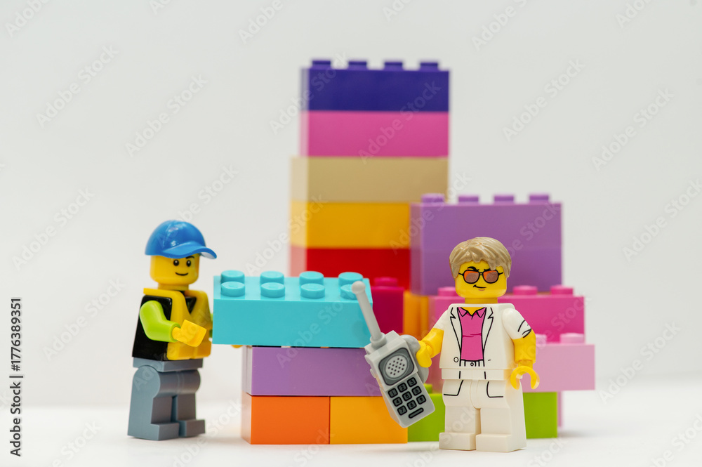 Naklejka premium A miniature LEGO man: A businessman with a mobile phone and a construction worker stand next to LEGO bricks on a white background.