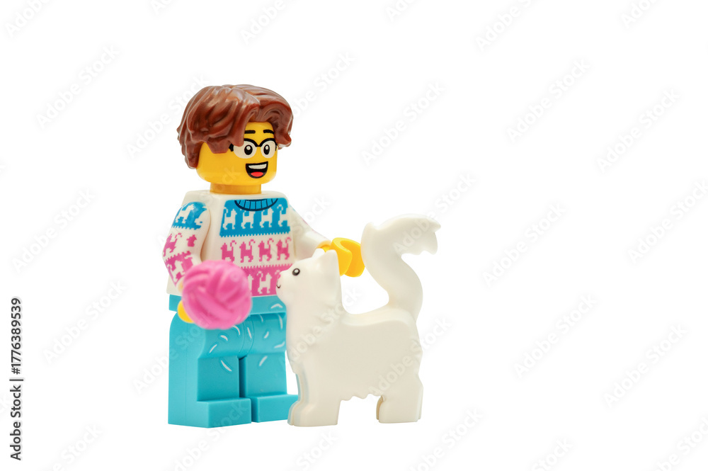 Naklejka premium A minifigure LEGO man: Animal lover playing with a cat tossing a ball on a white background.