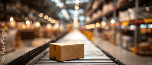 A cardboard box on a conveyor belt in the middle of an industrial warehouse with blurred lights and shelves behind it