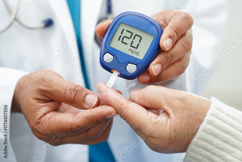 Asian doctor using digital glucose meter for check sample blood sugar level to treatment diabetes.