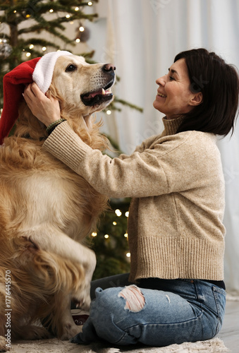 Happy Woman Hugs Dog Wearing A Santa Hat At Christmas Holidays