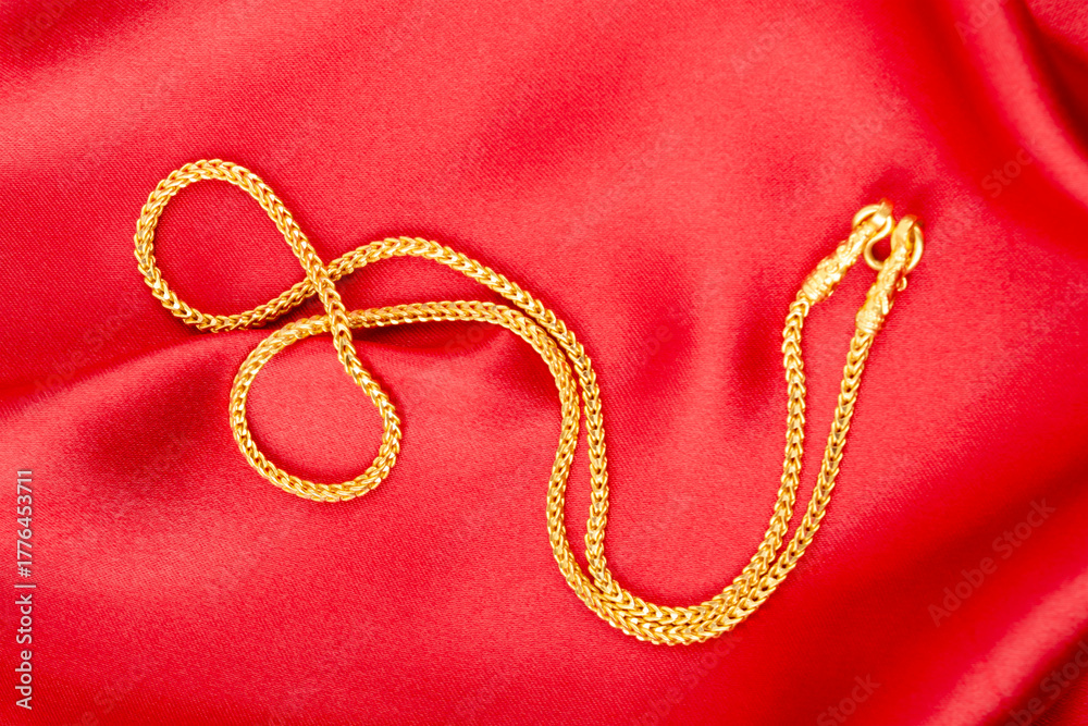 Fototapeta premium Gold chain necklace on red silk textile.