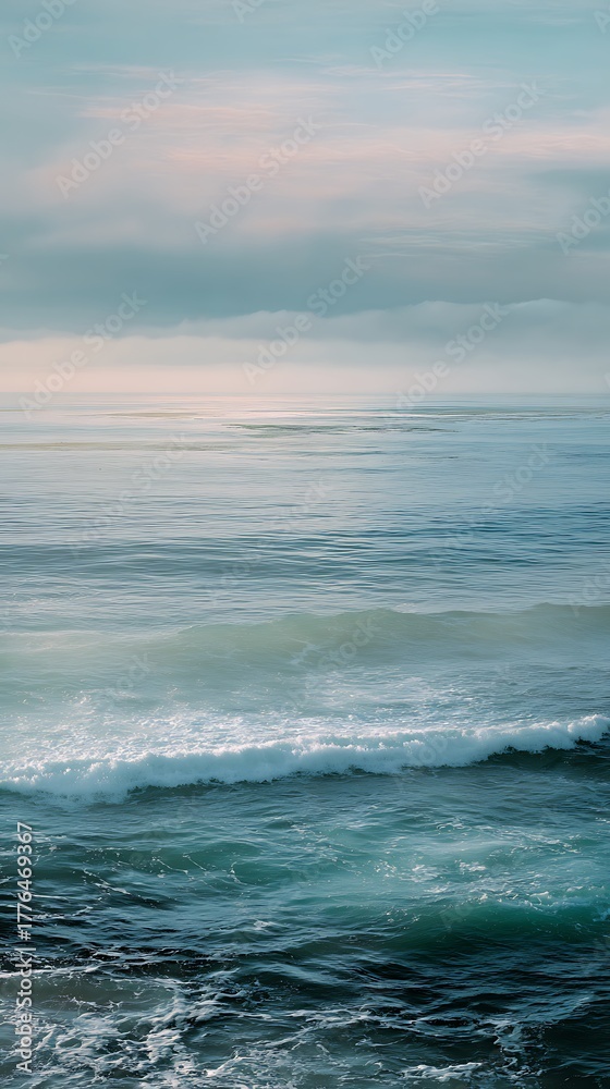 Fototapeta premium Blue ocean water with foamy waves under a calm cloudy sky horizon.