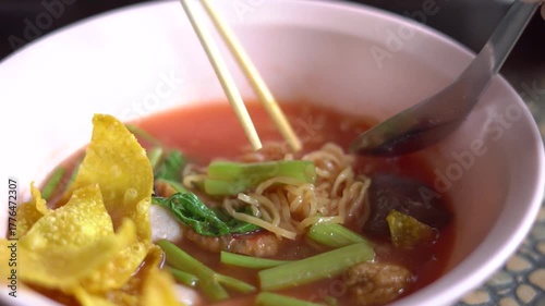 A bowl of Thai Yen Ta Fo noodle soup with pink broth, fish balls, fried wonton, morning glory, and tofu served in a pink bowl. A popular street food dish in Thailand known for its unique sweet and sou