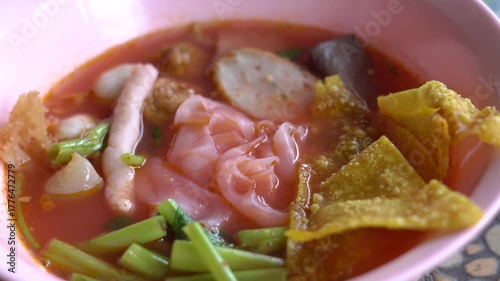 A bowl of Thai Yen Ta Fo noodle soup with pink broth, fish balls, fried wonton, morning glory, and tofu served in a pink bowl. A popular street food dish in Thailand known for its unique sweet and sou