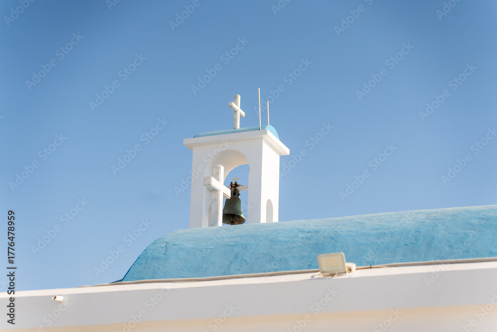 Fototapeta premium The bright blue roof of a historic church stands out against the clear sky. A bell and cross adorn its tower, highlighting its architectural beauty and cultural significance.