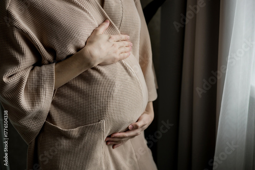 Close up of pregnant female with arms on her round belly.