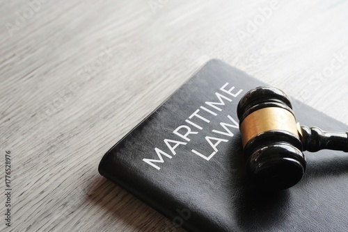 A gavel on a black law book titled MARITIME LAW. Justice, regulation of shipping, and the legal aspects of the sea concept.
