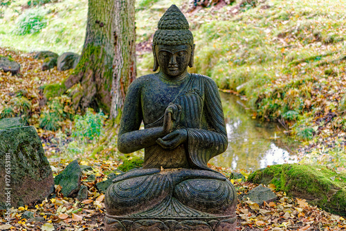 Praying Buddha stone statue in peaceful park landscape meditative spiritual atmosphere calm nature scene with ancient inspired sculpture and serene mood