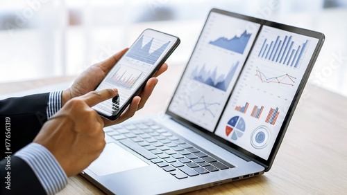 Close up of a businessman analyzing financial data on a laptop and smartphone, showcasing business intelligence and analytics