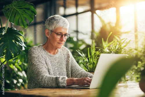 Senior Woman Working on Laptop Surrounded by Indoor Plants in Sunlit Room.