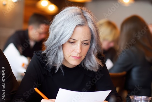 Focused Woman with Gray Hair Reviewing Documents in a Busy Modern Office.