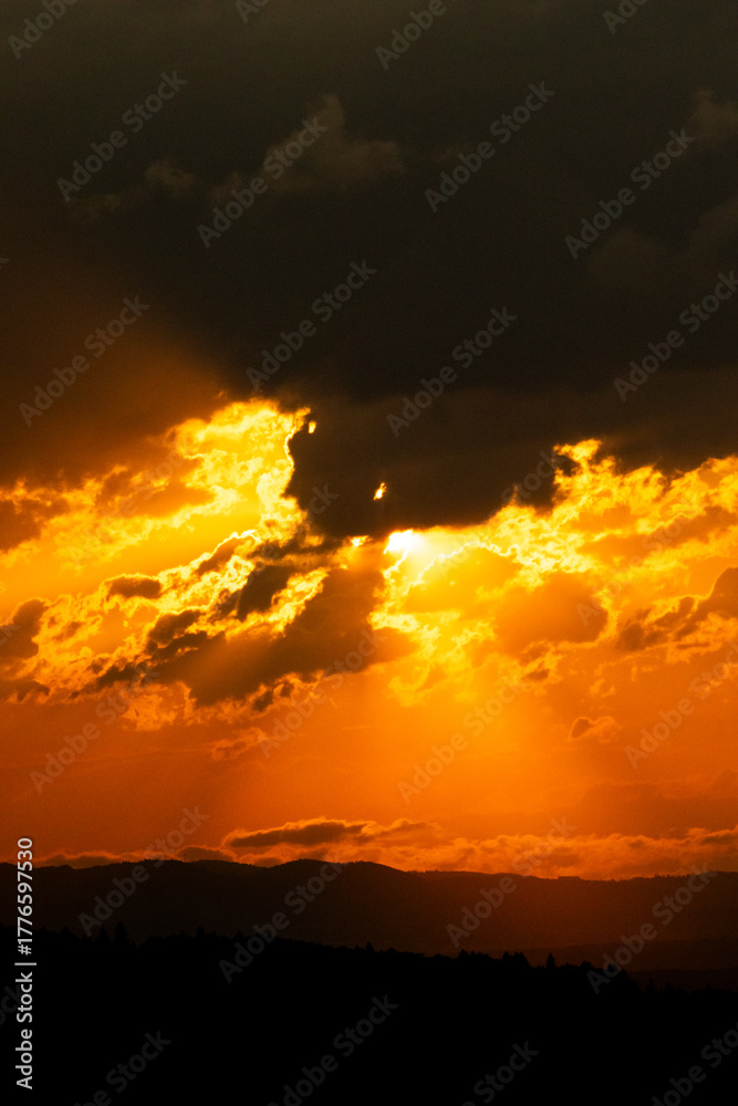 Fototapeta premium Fiery orange sunset sky with dramatic clouds and glowing sunlight