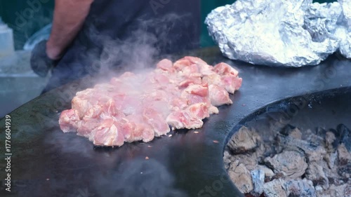 Large pork pieces sizzle on open flame grill during street food meat preparation in outdoor cafe setting showcasing traditional cooking method