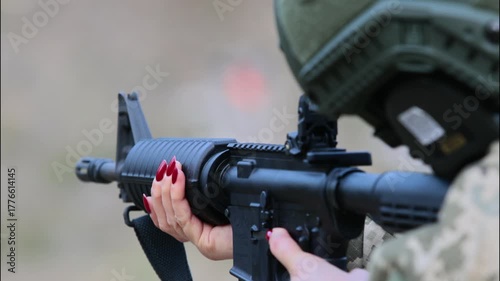 A female soldier with red nails aims a rifle. Concept for empowerment, duality, and modern defense