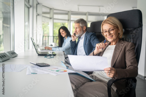 Foto Three busy happy middle aged professional business man and two women executive leaders team using laptop working on computer at work desk having conversation on financial project at meeting in office