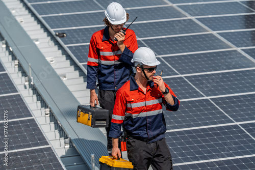 Solar engineer teamwork maintenance energy rooftop technician with helmet tool box radio communication inspection under sunlight on panel field showing focus and safety during routine service