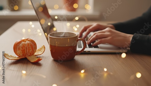 Person typing on laptop with steaming cup and decorative lights
