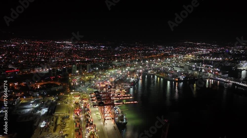 Incredible aerial view of mersin's bustling commercial port lit up at night, featuring brightly lit cranes, rows of containers, and a cargo ship being loaded and unloaded