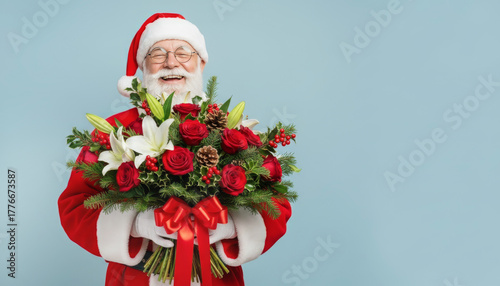 Cheerful Santa Claus waist-up presenting elegant bouquet of red and white flowers with pine cones and fir branches, blue pastel background, winter holidays, flower shop and festive greeting designs