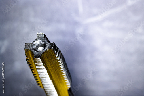 Close-up view of a metal thread tap showing detailed cutting edges and grooves. The precision tool is used for creating internal threads in metalworking and engineering applications.