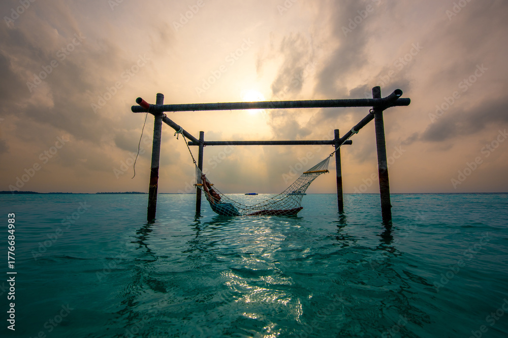Fototapeta premium Tranquil closeup calm sea water waves with palm trees. Model sitting on hammock. Tropical island beach landscape exotic shore coast. Summer vacation, holiday amazing nature. Relax paradise, Maldives.