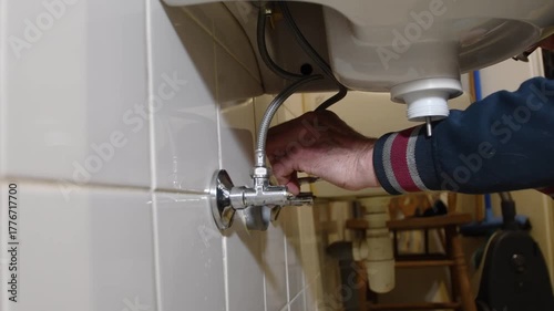 Professional plumber's hand turning an angle stop valve to shut off the water supply to a bathroom sink before starting repairs, ensuring a safe and dry working environment for plumbing maintenance