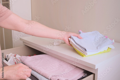 woman places neatly folded children's clothes into the top drawer of a white dresser