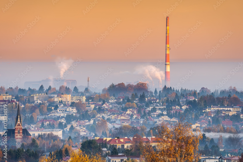 Fototapeta premium Industrial sunrise: smoke from power plant and waste incinerator chimneys over provincial polish city in autumn orange hues. CO2, pollution, ETS, European Union and its requirements