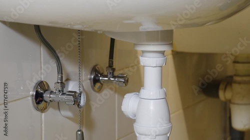 Professional plumber hands turning a chrome shut off valve under a white ceramic bathroom sink to stop the water flow before starting plumbing repairs, preventing leaks and property damage