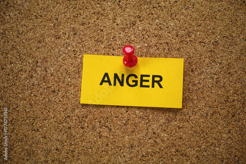 A yellow paper note with the word Anger on it pinned to a cork board. Close up.
