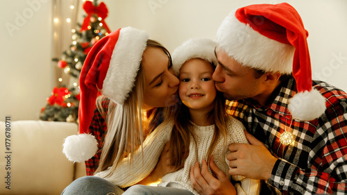 Mother, father, and daughter sitting together in Santa hats, parents kissing their smiling child on the cheeks, celebrating Christmas with warmth, joy, and love at home.