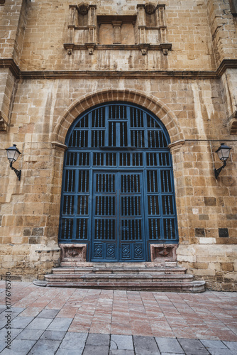 Wallpaper Mural Large arched blue wooden door set in a weathered stone facade of a historic Oviedo building, with carved detail, wall lanterns and worn steps — dramatic architectural entrance Torontodigital.ca