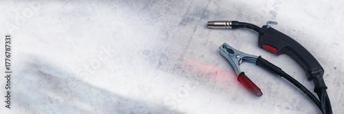 Принти на полотні Close-up of professional MIG MAG welding torch welding gun and a copper ground clamp earth clamp resting on a metallic, scratched workbench or surface