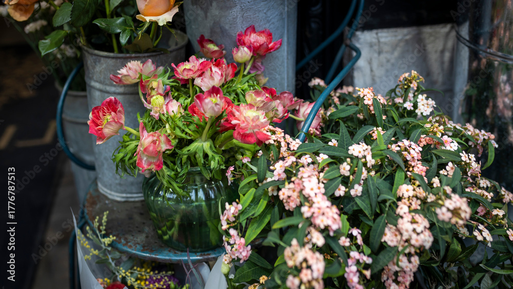 Fototapeta premium Red anemones and buttercups in a round glass vase on a metal chair, with a bouquet of orange roses for interior decoration on special occasions like weddings, dates, and funerals.