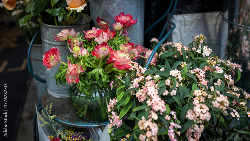 Red anemones and buttercups in a round glass vase on a metal chair, with a bouquet of orange roses for interior decoration on special occasions like weddings, dates, and funerals.