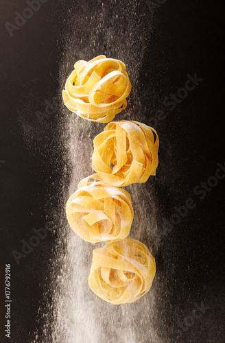 twisted pasta falling down and flour falling on a black background