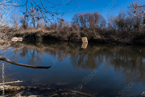 ose view of an old mossy concrete block partially submerged in water, reflected on a calm river surface
