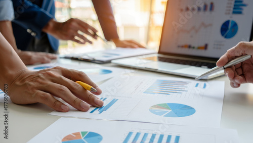 Business team gathered at a desk reviewing financial charts, reports and laptop data, collaborating on analysis, planning and strategy to assess company performance and growth