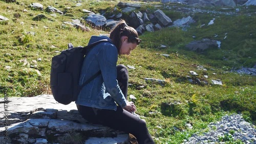 A young woman with a backpack in the mountains, sat down on a rock to tie her shoelaces and relax. Walking in the mountains, hiking.