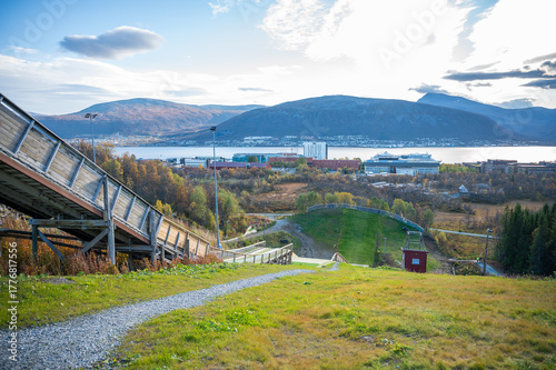 Gronnasen Hoppsenter, Tromso, scenic view of a ski jump with a wooden ramp, set against a backdrop of mountains, a body of water, and a cityscape