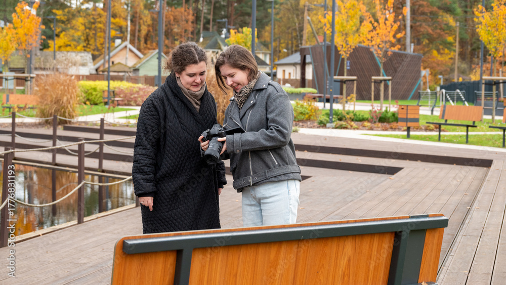 Fototapeta premium Two Friends Share a Moment in a Park While Reviewing Photos on a Camera During Fall