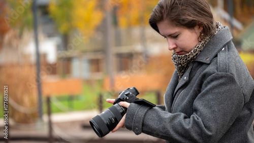 Young Woman Examining Camera Settings in a Park During Autumn