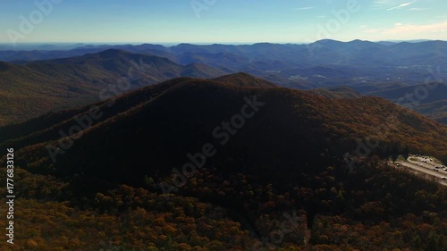 A cinematic 4K aerial of the Brasstown Bald summit , a popular state park shot during golden hour and during fall with light casting rays and shadows over the rolling hills of the Blue Ridge mountain 