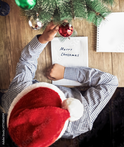 A guy in a Santa Claus hat holds a Christmas tree decoration