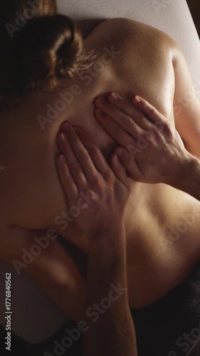 A woman receives a back massage, her skin glistening with oil. The masseuse's hands knead her shoulders and back, providing relaxation and relief.