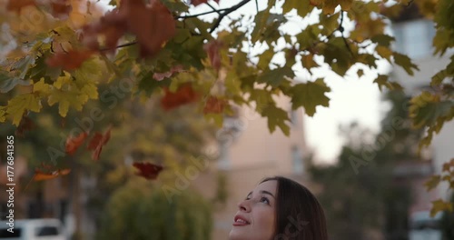 Young woman throwing yellow autumn leaves up, slow motion